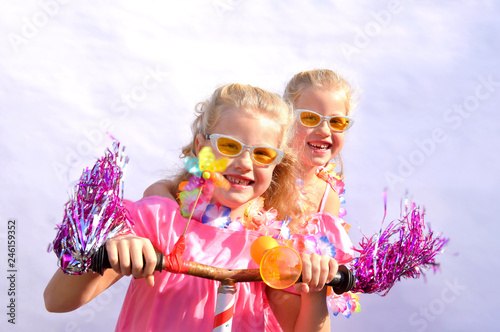 Twin sisters play together riding an imaginative bicycle. They use a rusty handlebar they found in the garage. They fit it with fringes, a windmill and an orange plastic horn.