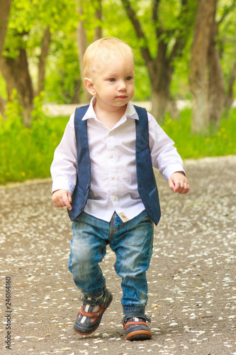 Toddler boy in a trendy stylish suit walks along the path in the spring park.