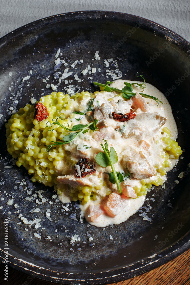 Risotto with porcini mushrooms, sauce, sun-dried tomatoes and pea sprouts on a beautiful clay deep dish of gray color Risotto with porcini mushrooms, sauce, sun-dried tomatoes and pea sprouts on a beautiful clay deep dish of gray color