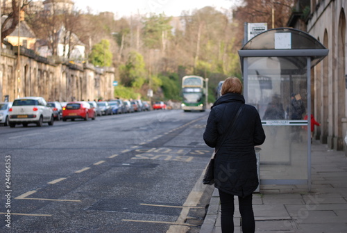 A woman in black dress is waiting for a bus in front of bus stop