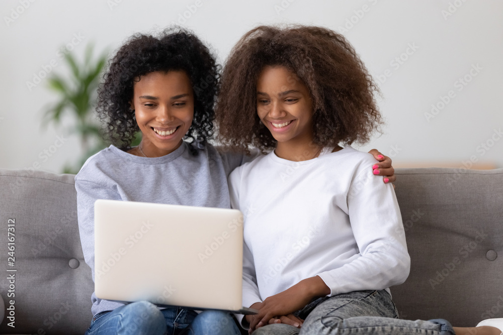 Www Amrican Mom Hd Vedios - Foto de Smiling African American mother and daughter sit on couch watching video  on laptop, black millennial nanny hang out with teen girl, relax on sofa  using computer, mom and kid rest