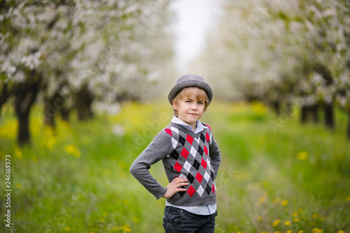 Portrait of a boy in a hat standing against a background of flowering trees
