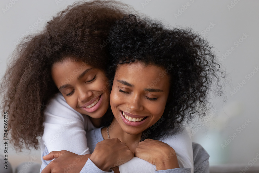 Sweet teenage daughter hug young African American mom from behind showing love and care, tender teen girl embrace mother or nanny, parent and child have close intimate moment together Sweet teenage daughter hug young African American mom from behind showing love and care, tender teen girl embrace mother or nanny, parent and child have close intimate moment together