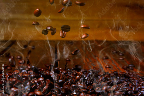 roasted coffee beans falling on stack, hot and smoky. Rustic wood background blurred