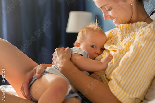 Young mother, sitting in bed with her baby boy, having shared moment of joy, breastfeeding, hugging, kissing, cudling photo