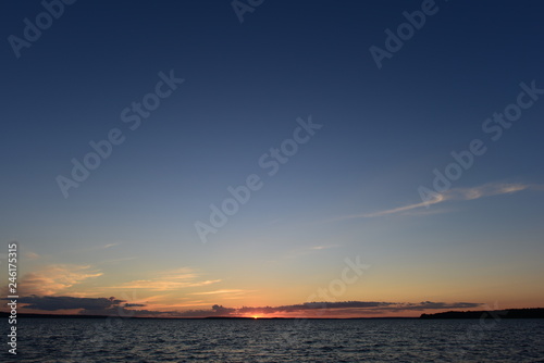 Sunset is a small bright point on the horizon the sun is infinite in space the blue of the sky and the water of the lake