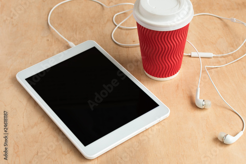 Tablet with blank black screen with earphones and a cup of coffee top view. Office morning concept. Wireless technology.