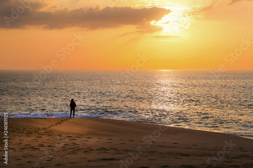 Woman stands on the ocean and looks at the sunset.