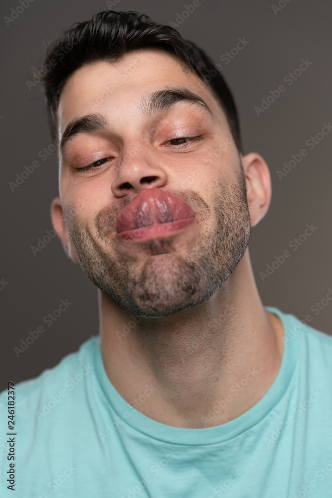 Handsome caucasian white male with black short hair and stubble with light blue t shirt tongue touching nose