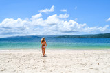 young lady walking in bikini on the beach to the ocean, idyllic island with white beach and turquoise ocean