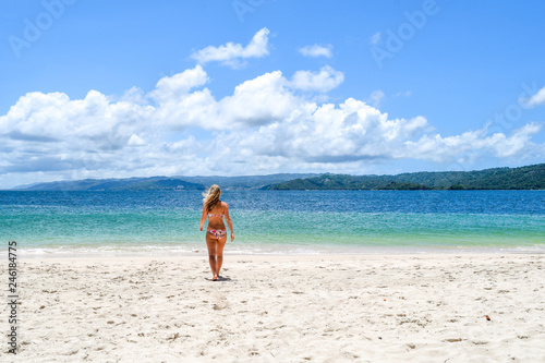 young lady walking in bikini on the beach to the ocean, idyllic island with white beach and turquoise ocean