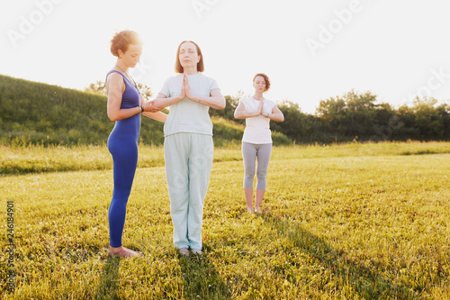 Mother and two young daughters do yoga oh in the park on a sunny summer day. Concept of health and longevity at any age