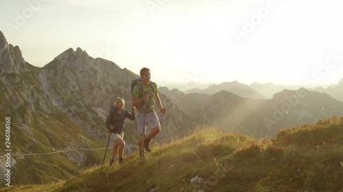 SLOW MOTION SUN FLARE: Happy Caucasian woman and man enjoying a hike in the stunning mountains of Slovenia. Carefree tourist couple having fun trekking in the tranquil Alps on a sunny summer afternoon