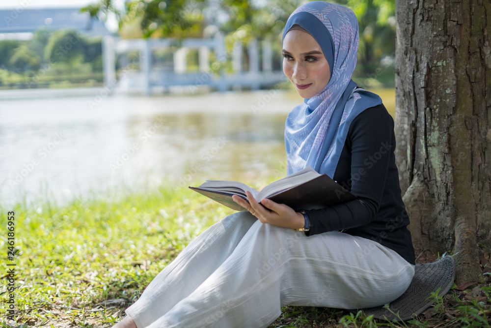 Obraz premium Happy Asian woman reading book under the tree lakeside.