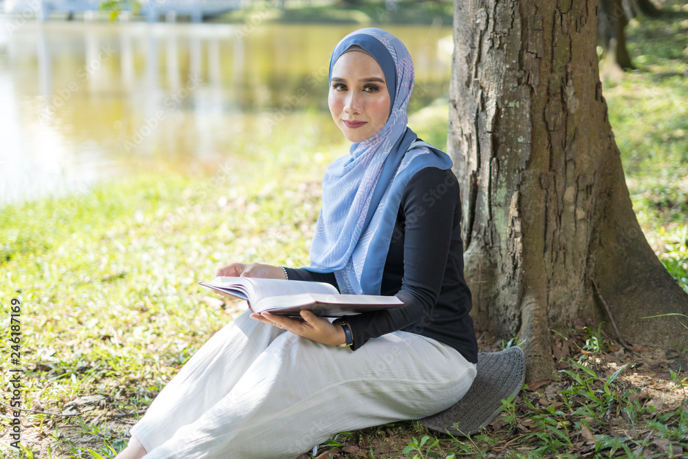 Happy Asian woman reading book under the tree lakeside. Happy Asian woman reading book under the tree lakeside.