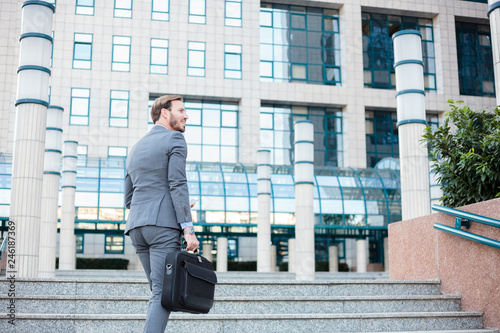 Successful young businessman climbing the steps in front of an office building, carrying a briefcase