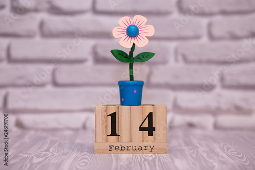 February 14. Day 14 of month on wooden calendar with toy flower on white brick background. Happy Valentines day. Love concept.