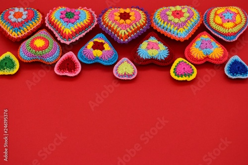 Knitted hearts of colored yarn on a red background. Valentine's Day, love, handmade, amigurumi, hobby, decoration, postcard, creative.