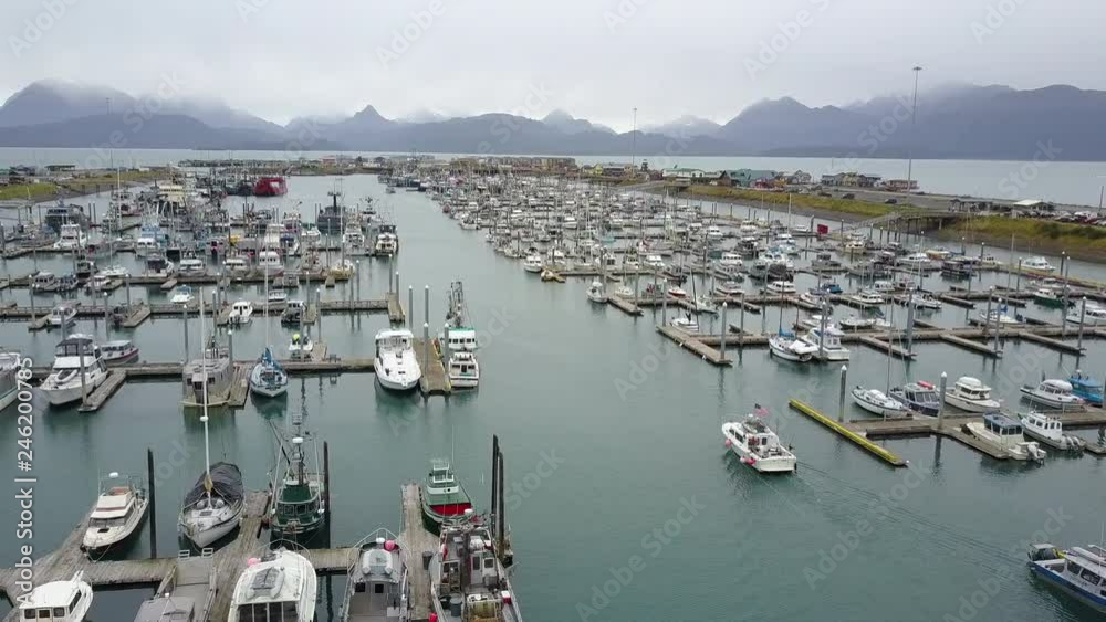 Aerial shot flying over the busy boat harbor in the beautiful small city of Homer, Alaska, with a magnificent backdrop in the distance