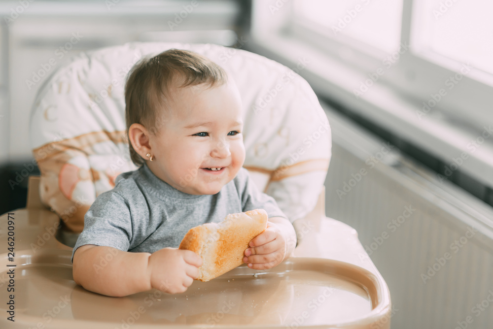 baby in the kitchen in the high chair there is a piece of bread baby in the kitchen in the high chair there is a piece of bread