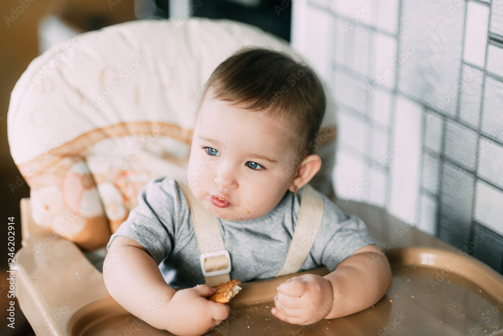 Fototapeta premium little girl in a high chair eating cookies