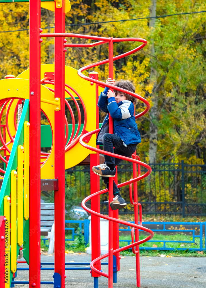 Kid having fun at playground in autumn. Modern colorful playground in a warm day. Kids fashion. Kids activities. Autumn holidays. Cute boy playing outdoor. Child wearing a warm blue jacket.