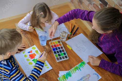 Happy children - boy and two girls is drawing with colorful paint