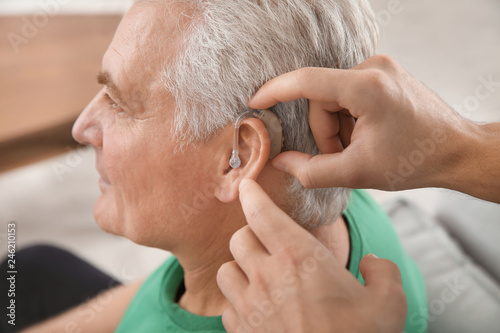 Young man putting hearing aid in father's ear indoors, closeup