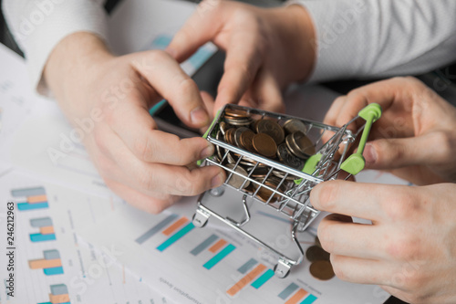 Men's hands pulled in different directions Dummy shopping cart filled with coins