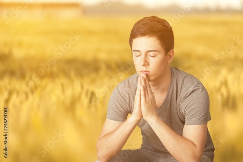 Young man praying against grey background