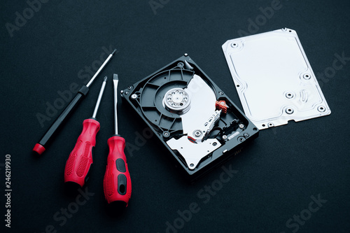 Data storage hard disk drive uncovered with assembly case cover part and screwdrivers, Computer hardware repair concepts.
