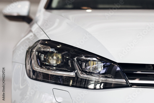 Closeup headlights of a modern white color car. Detail on the front light of a car. Modern and expensive car concept. The car is in the showroom