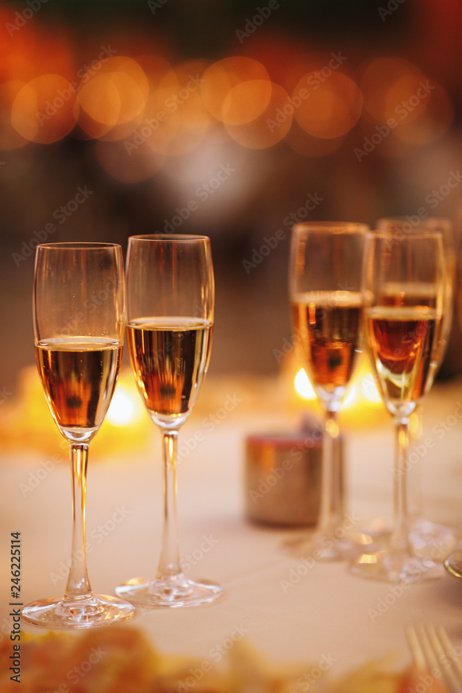 Four glasses with pink champagne stand on the table with shiny candles