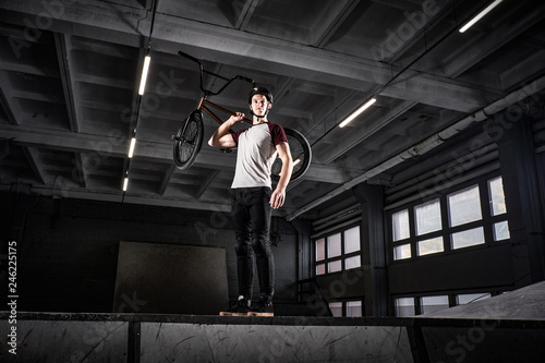 Wallpaper Mural Full body portrait of a BMX rider holding his bike on shoulder and looking away in a skatepark indoors Torontodigital.ca