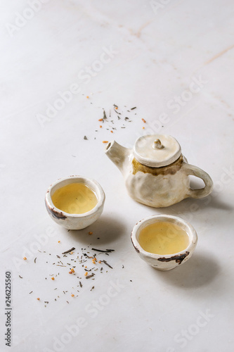Hot green tea in two traditional chinese clay ceramic cup and teapot standing on white marble table.