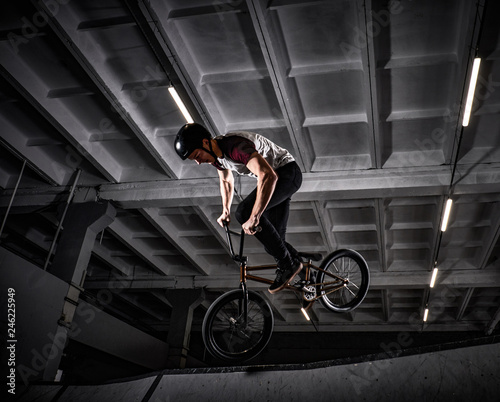 Professional BMX rider in protective helmet performing tricks in skatepark indoors