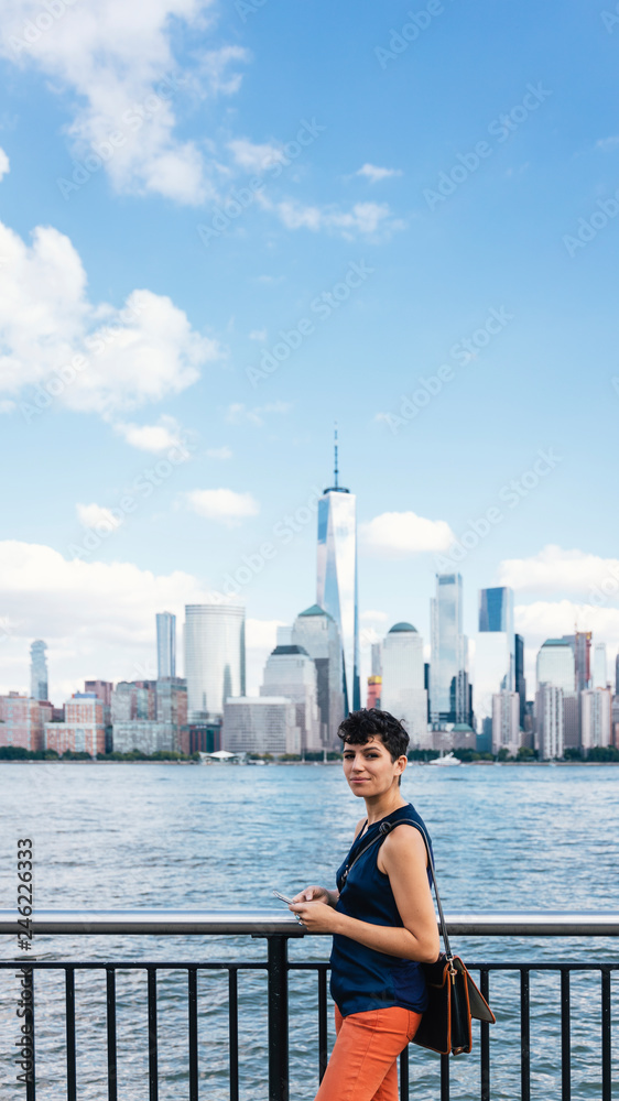 Portrait of woman using smart phone while standing on promenade by river against sky in city Portrait of woman using smart phone while standing on promenade by river against sky in city