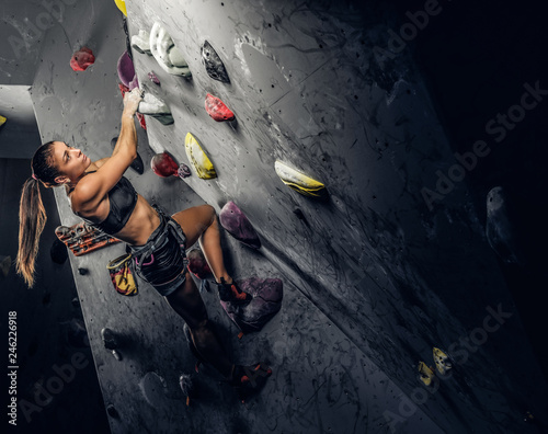 Young sporty woman climbing artificial boulder indoors.