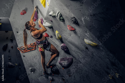 Young sporty woman climbing artificial boulder indoors.