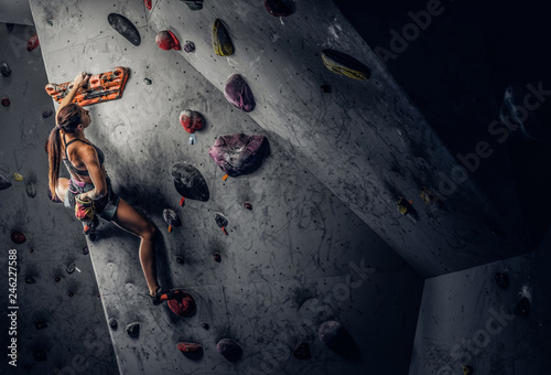 A young woman wearing sportswear practicing rock-climbing on a wall indoors