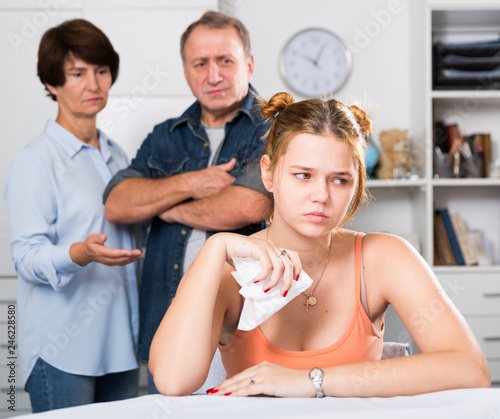 Parents are sympathying their sad daughter who is sitting at the table