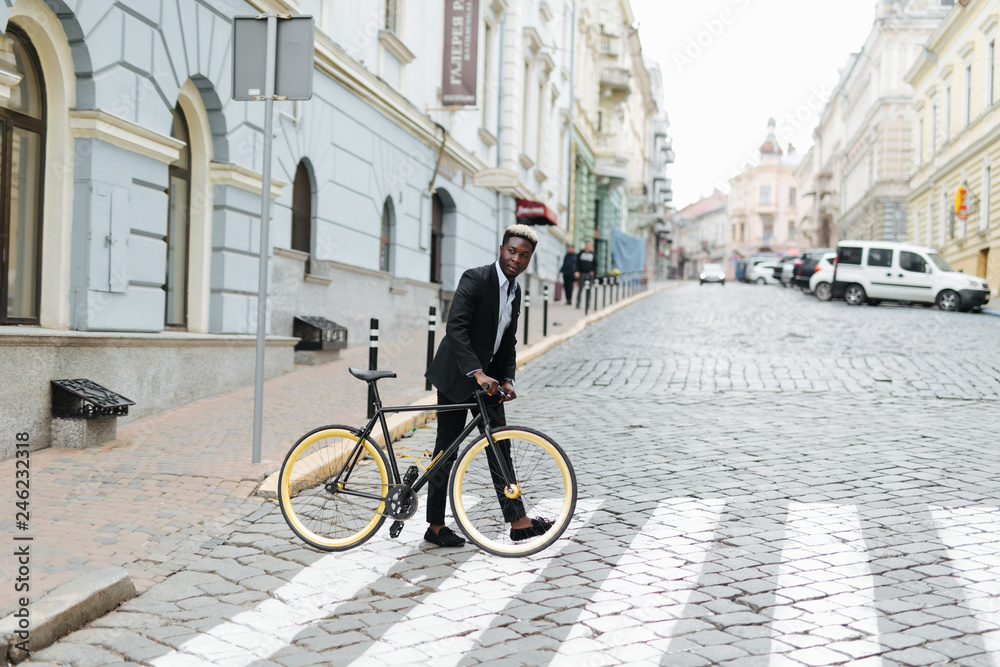 People, style, city life and lifestyle. Young handsome african hipster man in suit and fixed gear bike crossing crosswalk on street