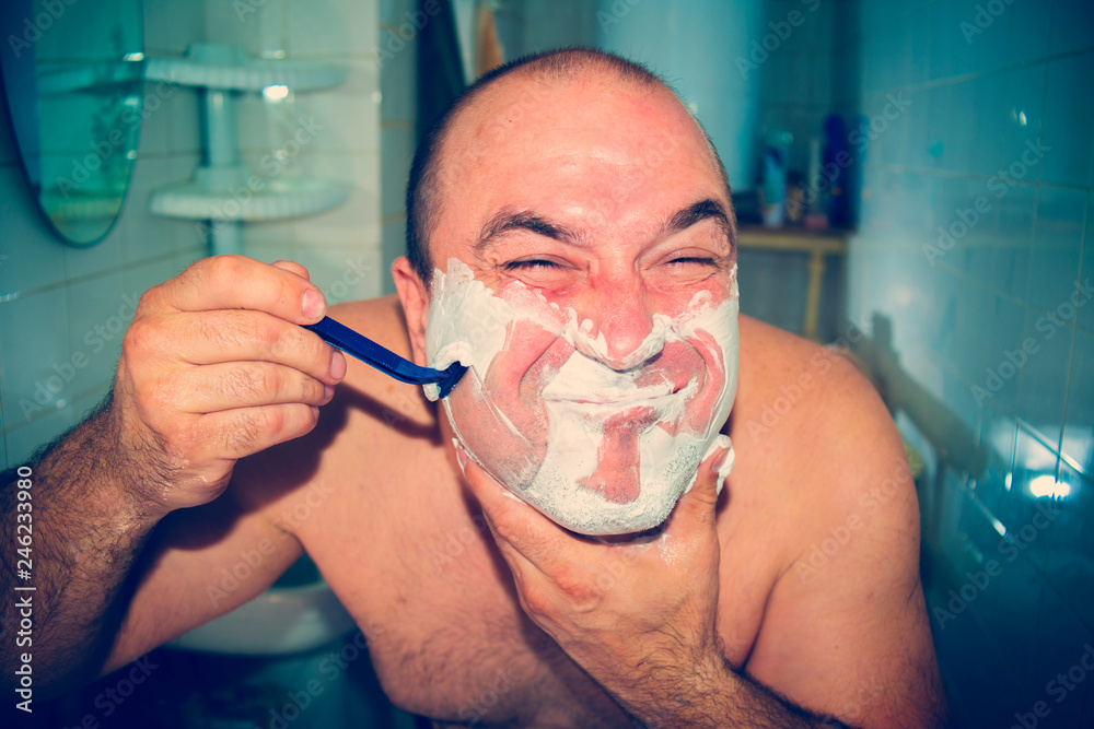 Crazy and insane man shaves in the bathroom, wide-angle photo.