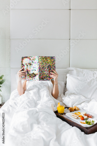 Woman having breakfast in bed and reading magazine photo