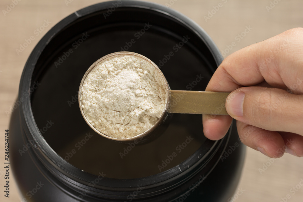 Whey Protein. Perspective of person preparing protein shake.  Vanilla flavour.  Wooden background.