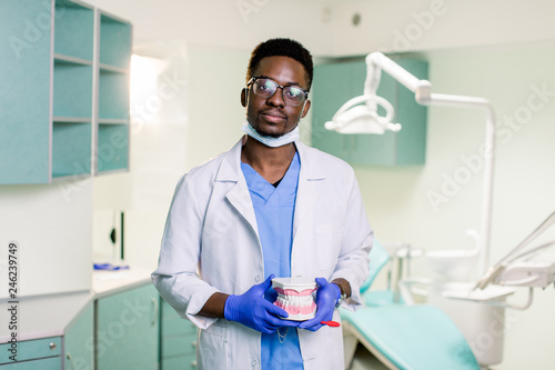 Black dentist in a dental clinic holds artificial jaws in his arms