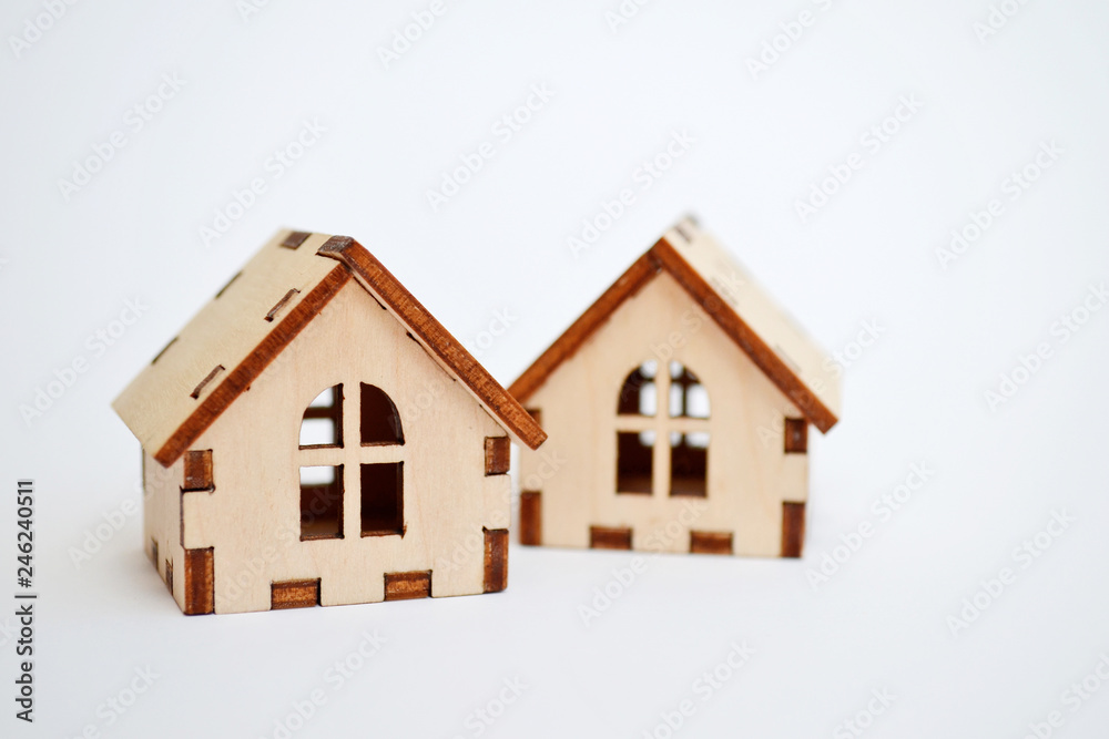 Two wooden toy houses on white background, one house stands behind the other, concept for selling houses with copyspace