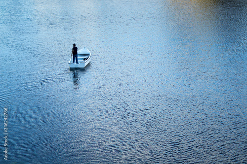 Homem solitário a navegar calmamente num pequeno barco branco photo