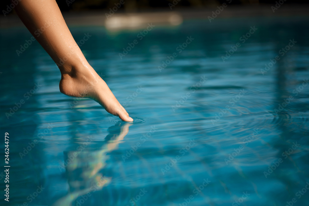Closeup young female leg touch blue water in swimpool