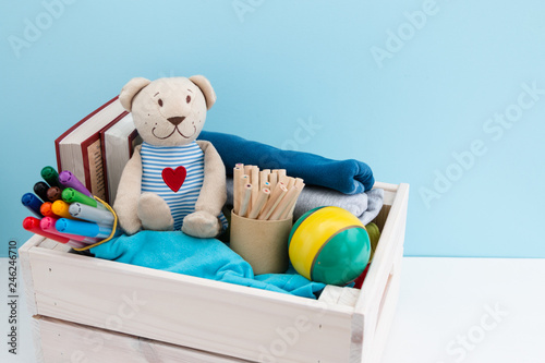 Wooden box with donations: children's toys, stationery and children's clothing. Concept: you can help, they need help. Background, free space for inscription. Red heart on the chest of a teddy bear.